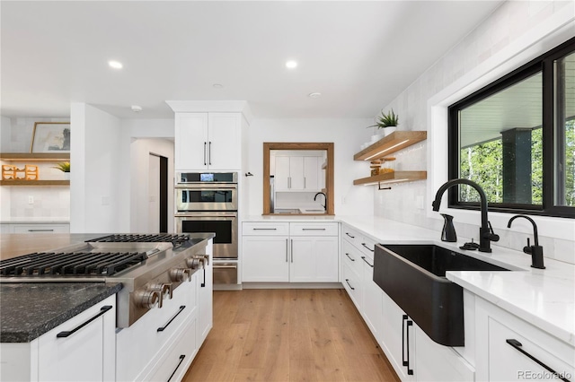 kitchen featuring sink, dark stone countertops, appliances with stainless steel finishes, white cabinets, and light wood-type flooring