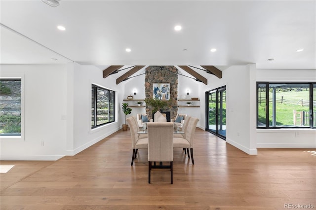 dining room with a fireplace, lofted ceiling with beams, and light wood-type flooring