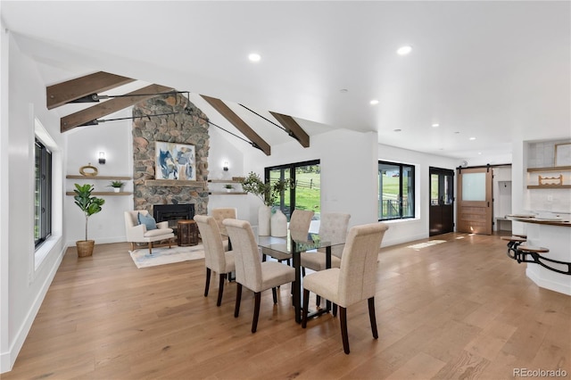 dining area with vaulted ceiling with beams, a fireplace, light hardwood / wood-style floors, and a barn door