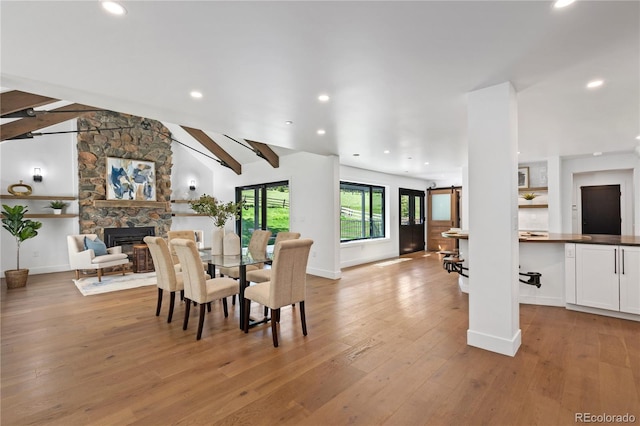 dining space with vaulted ceiling with beams, light hardwood / wood-style flooring, and a fireplace