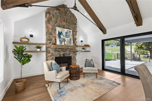 sitting room featuring a stone fireplace, beamed ceiling, wood-type flooring, and high vaulted ceiling