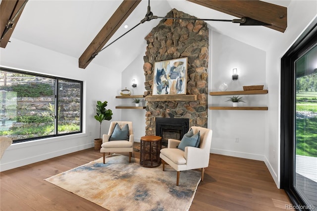 living area featuring lofted ceiling with beams, hardwood / wood-style flooring, a stone fireplace, and ceiling fan