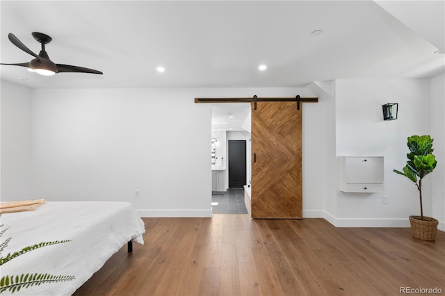 bedroom with wood-type flooring, a barn door, ensuite bathroom, and ceiling fan