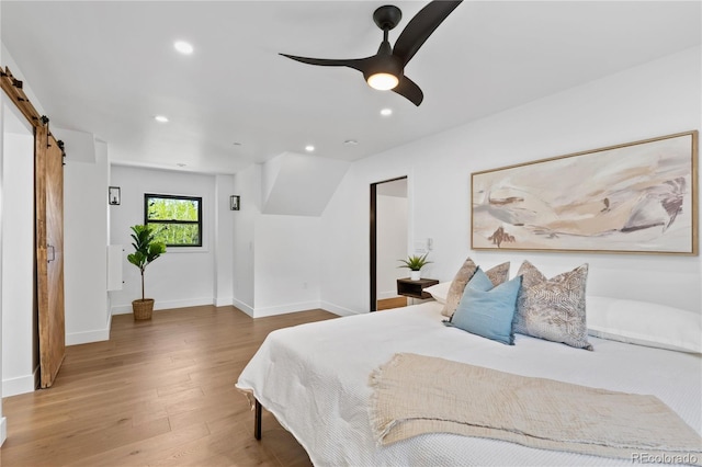 bedroom featuring ceiling fan, a barn door, and wood-type flooring