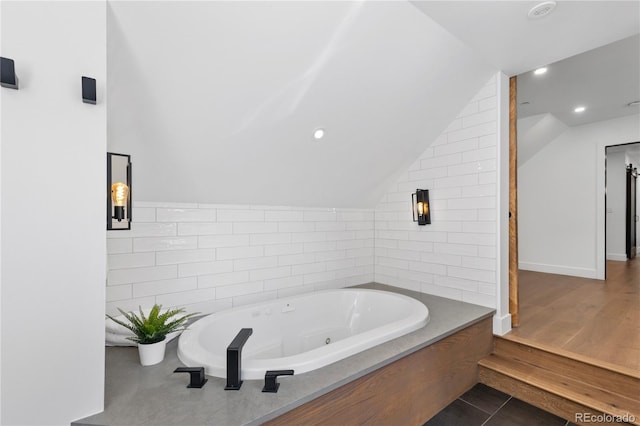 bathroom featuring hardwood / wood-style floors, vaulted ceiling, and a bathing tub