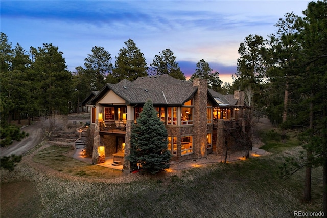 10231 Democrat Rd, Parker, CO 80134 - back of property at dusk with stone siding, a chimney, stairway, a patio area, and a deck