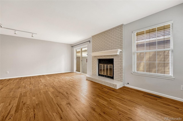 unfurnished living room with hardwood / wood-style floors, brick wall, track lighting, and a fireplace