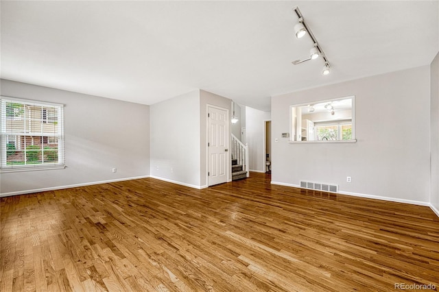 unfurnished living room featuring rail lighting and wood-type flooring