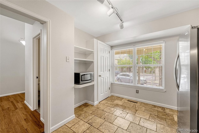 interior space featuring light tile patterned floors, stainless steel refrigerator, and track lighting