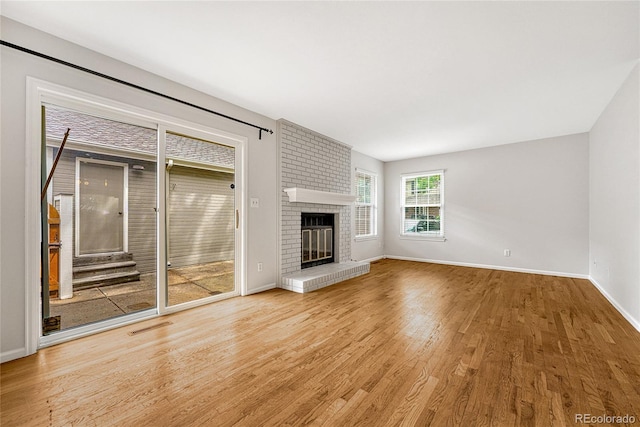 unfurnished living room featuring light hardwood / wood-style floors, brick wall, and a brick fireplace