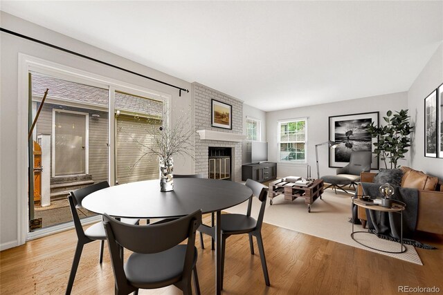 dining space with a fireplace, brick wall, and light hardwood / wood-style floors