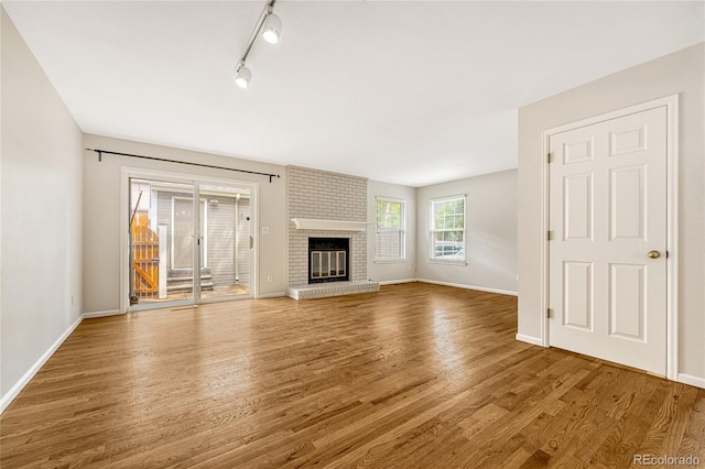 unfurnished living room with track lighting, a brick fireplace, brick wall, and wood-type flooring