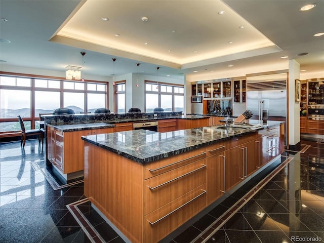 kitchen featuring a spacious island, sink, a raised ceiling, and dark stone counters