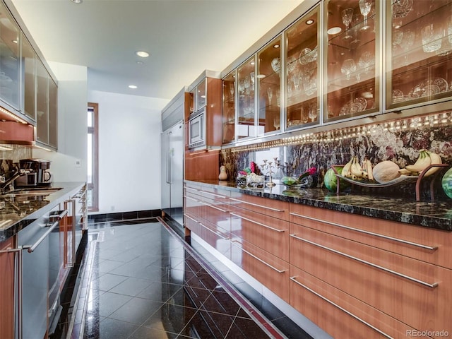 kitchen with built in appliances, dark stone countertops, tasteful backsplash, and sink