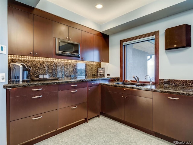 kitchen with dark stone countertops, tasteful backsplash, dark brown cabinets, and sink