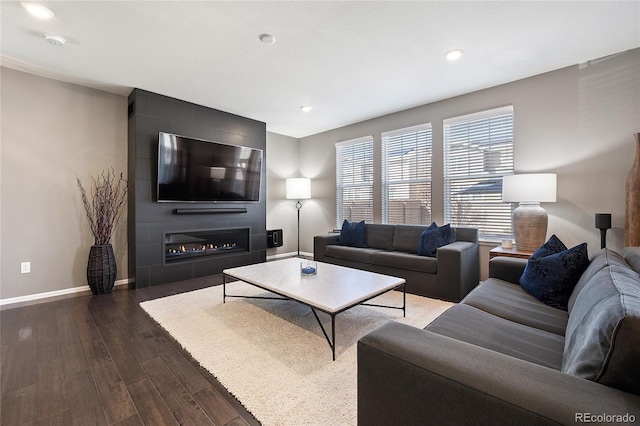 living area featuring recessed lighting, baseboards, a large fireplace, and dark wood-type flooring