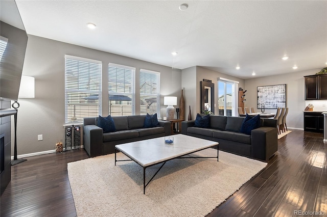 living area with a fireplace with raised hearth, baseboards, and dark wood-style flooring