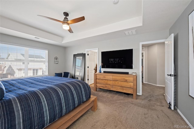 carpeted bedroom featuring a ceiling fan, a tray ceiling, baseboards, and visible vents