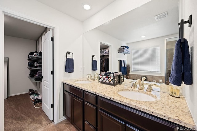 full bathroom with double vanity, a spacious closet, visible vents, and a sink