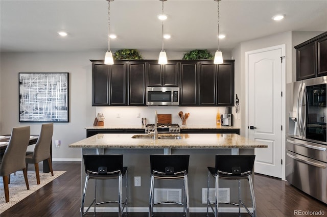 kitchen with dark wood-type flooring, appliances with stainless steel finishes, a sink, and light stone countertops