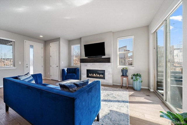 living area featuring a glass covered fireplace, baseboards, and light wood-style floors