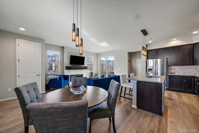 dining room with baseboards, a textured ceiling, light wood-style flooring, and a fireplace