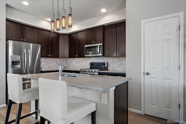 kitchen featuring a sink, dark brown cabinets, appliances with stainless steel finishes, pendant lighting, and light wood-type flooring