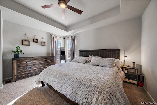 carpeted bedroom featuring ceiling fan, baseboards, and a tray ceiling