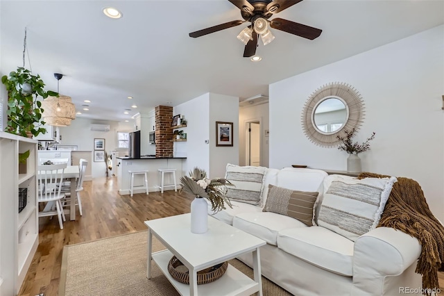 living room featuring an AC wall unit, ceiling fan, and light hardwood / wood-style flooring