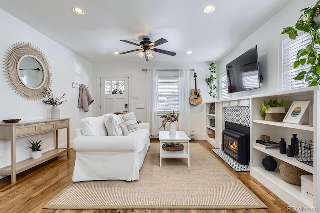 living room with a tiled fireplace, ceiling fan, and light hardwood / wood-style flooring