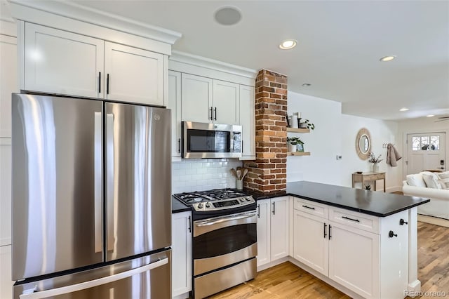 kitchen with light wood-type flooring, kitchen peninsula, white cabinets, and appliances with stainless steel finishes