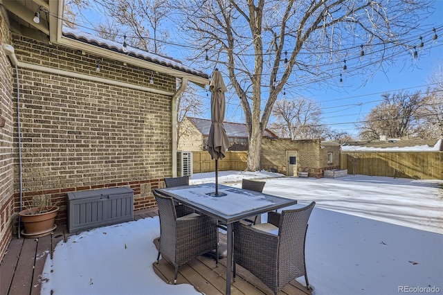 snow covered deck with a fenced backyard, an outbuilding, and outdoor dining space