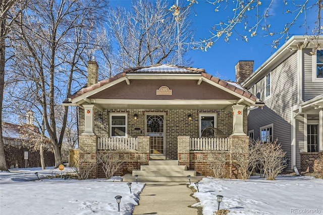 view of front of property featuring brick siding, covered porch, a chimney, and a tiled roof