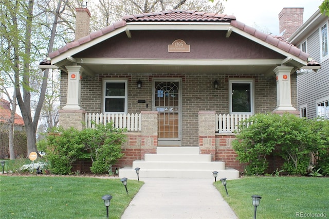 view of front of property with brick siding, a front lawn, covered porch, and a tile roof