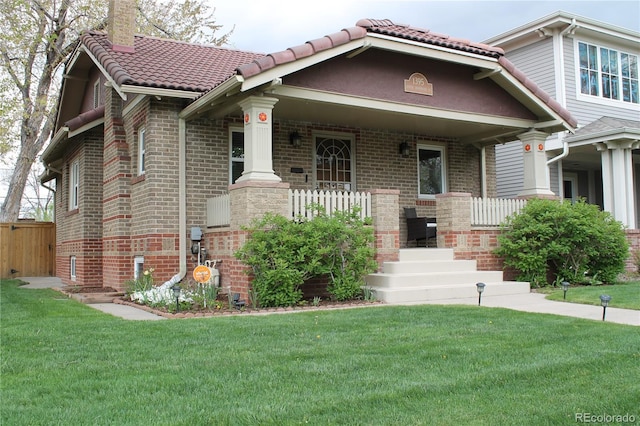 view of front of property with a porch, a front lawn, a chimney, and brick siding