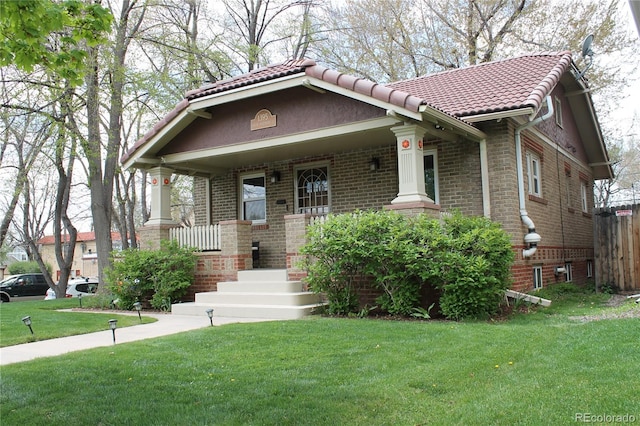 view of front of home with fence, a front lawn, brick siding, covered porch, and a tiled roof