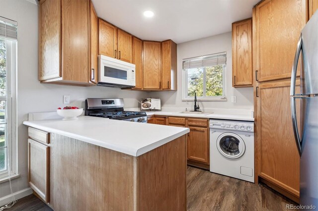 kitchen with stainless steel appliances, a peninsula, a sink, light countertops, and washer / dryer