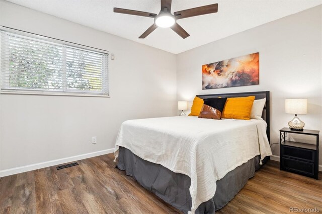 bedroom with a ceiling fan, wood finished floors, visible vents, and baseboards