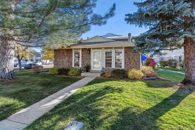 bungalow-style home with stone siding, a front lawn, and a chimney