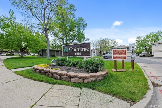 community / neighborhood sign with aphalt driveway and a lawn