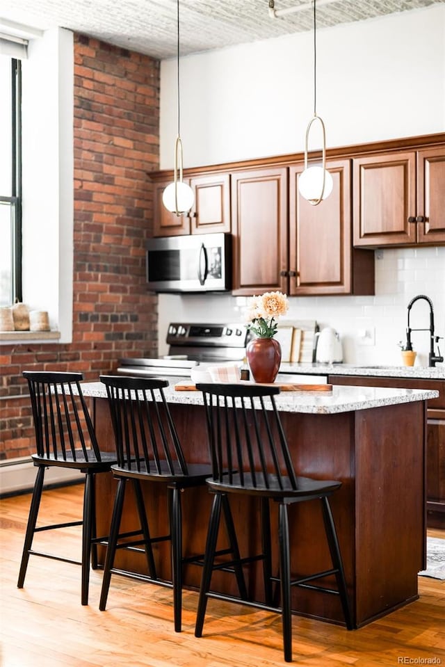 2261 Blake St Unit 2G, Denver, CO 80205 - kitchen featuring stainless steel appliances, light wood-style flooring, tasteful backsplash, hanging light fixtures, and a kitchen bar
