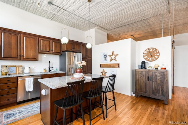 2261 Blake St Unit 2G, Denver, CO 80205 - kitchen featuring appliances with stainless steel finishes, a sink, a kitchen breakfast bar, decorative backsplash, and a center island