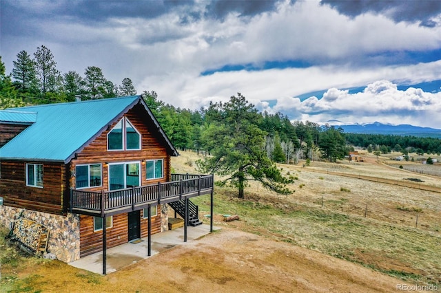 rear view of property with a patio, a deck with mountain view, stairs, log exterior, and metal roof