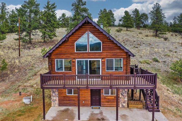 view of front facade with stairway, stone siding, a wooden deck, and a patio area