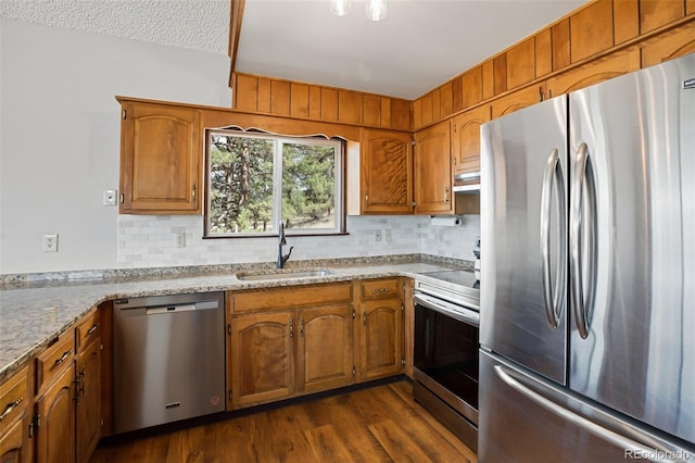 kitchen with backsplash, appliances with stainless steel finishes, brown cabinetry, and a sink