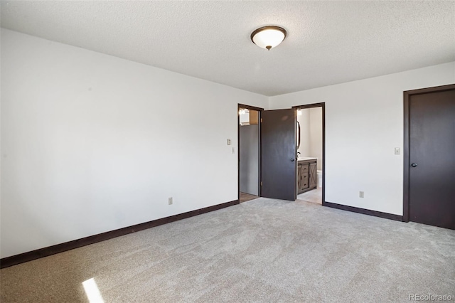 unfurnished bedroom featuring light colored carpet, a textured ceiling, baseboards, and connected bathroom
