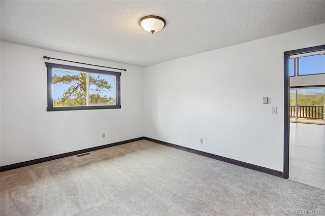 carpeted spare room with visible vents, a textured ceiling, and baseboards