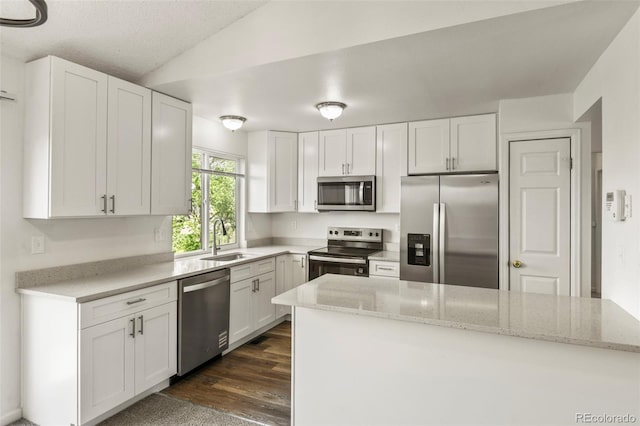 kitchen with stainless steel appliances, a sink, white cabinetry, lofted ceiling, and light stone countertops