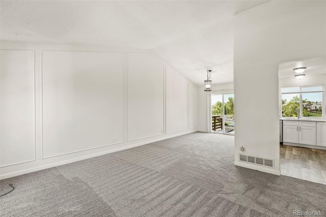 unfurnished living room featuring a decorative wall, carpet flooring, and vaulted ceiling