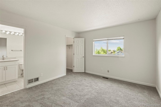 unfurnished bedroom featuring a textured ceiling, light carpet, a walk in closet, a sink, and baseboards